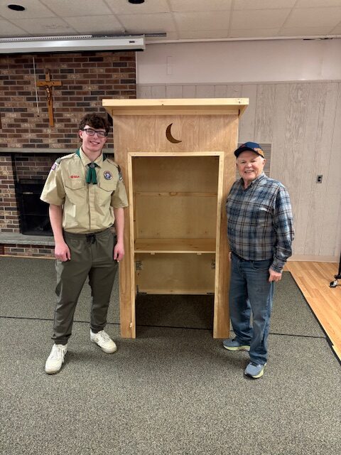 a photo of Pastor Joe and Lukas Ryan standing proudly in front of the newly-rebuilt outhouse