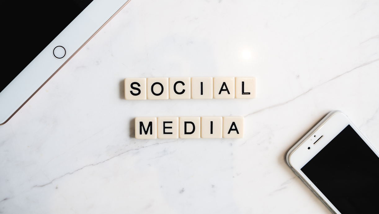 social media spelled out in game tiles on marble with a tablet and smartphone nearby